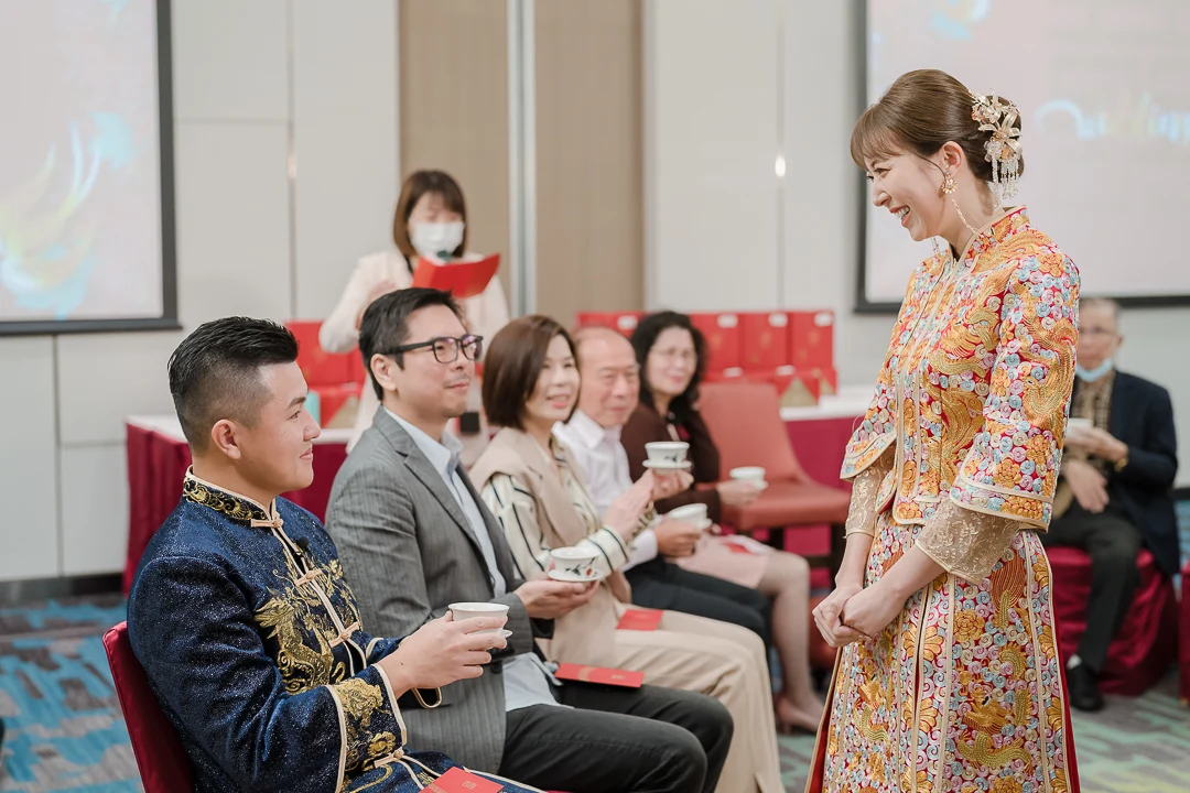 新娘與手持茶杯的新郎及親友相視微笑